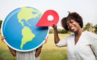 Une femme souriante tient un repère de localisation rouge à côté d'un grand globe terrestre : le référencement local