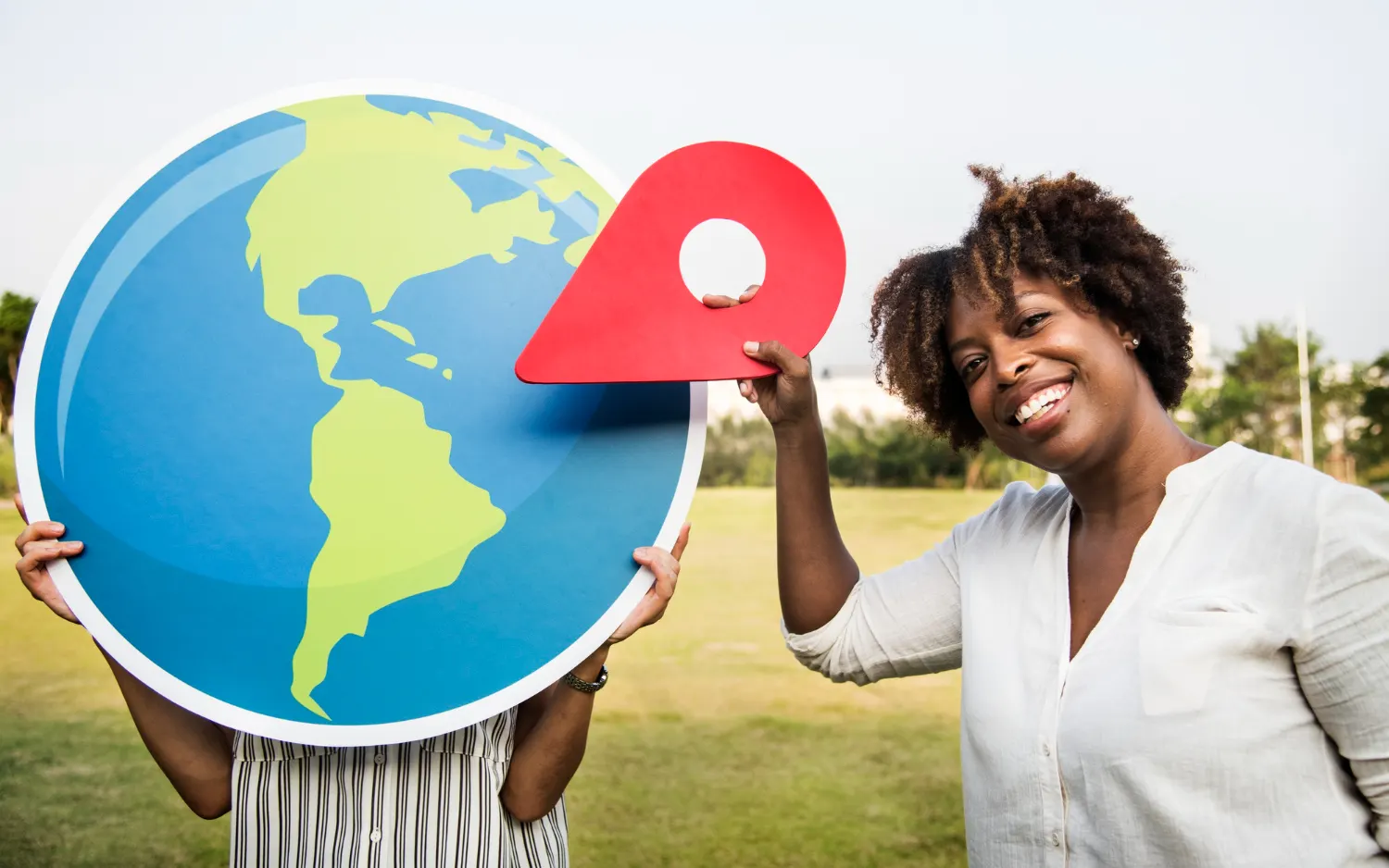 Une femme souriante tient un repère de localisation rouge à côté d'un grand globe terrestre : le référencement local
